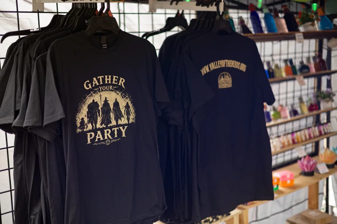 Black cotton Gather Your Party shirts displaying gold-toned fantasy adventurers on the front and Valley of the Nerds branding on the back.