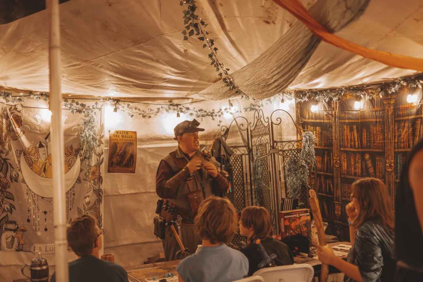 A costumed game facilitator guiding young participants through an adventure inside the event tent