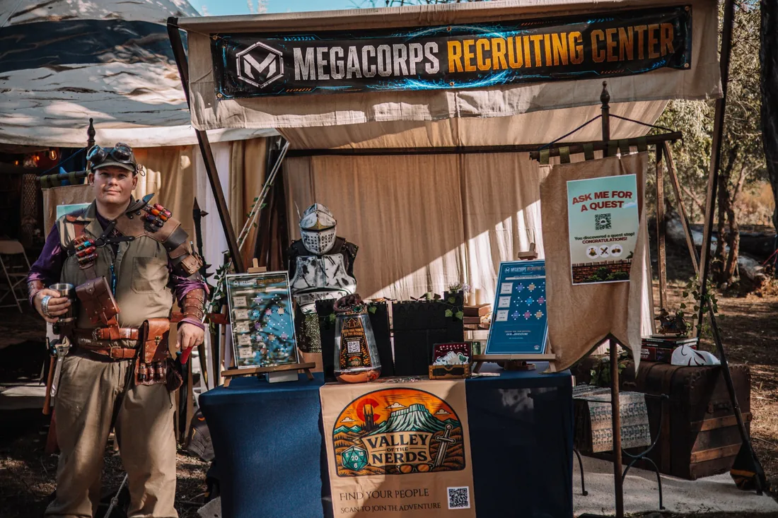 The Megacorps recruiting tent with a costumed participant, a Valley of the Nerds banner, quest signs and props.